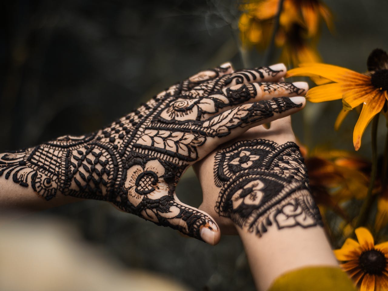 Close-up of beautifully decorated hands with henna designs surrounded by vibrant yellow flowers.