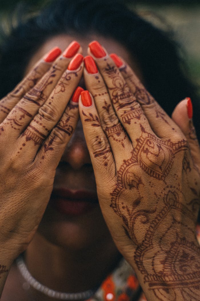 Close-up of a woman's hands with henna and red nail polish covering her face.