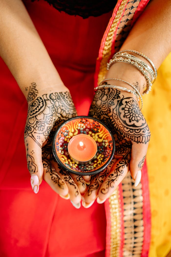 Beautiful mehndi decorated hands holding a lit candle during a Diwali celebration.